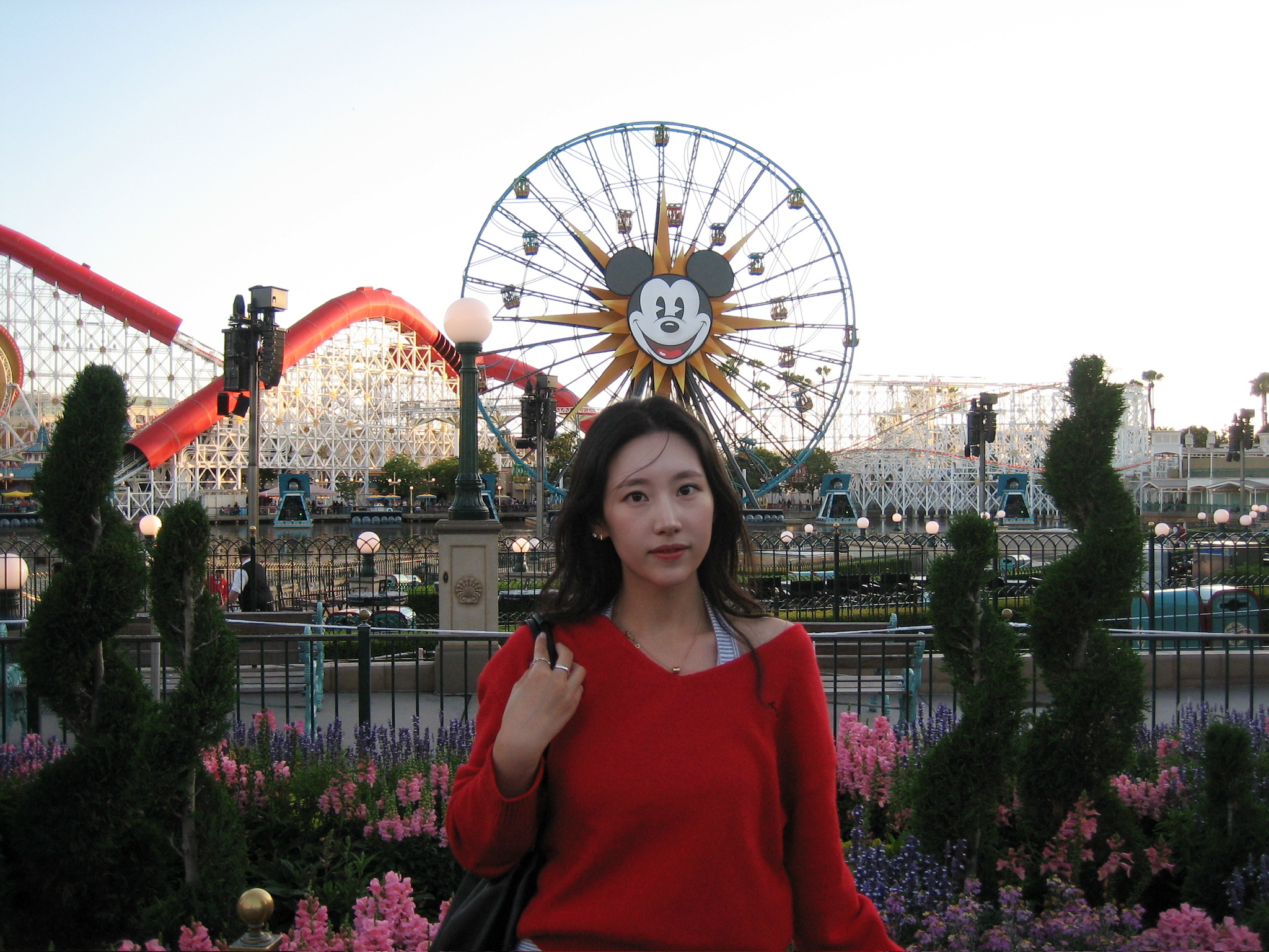 Esoo in a red sweater in front of a Ferris wheel at a theme park.